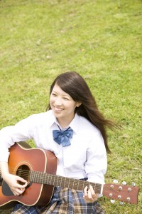 芝に座りギターを弾く女子高生